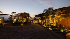 Un espacio exterior bien iluminado con escalones que conducen a un edificio, rodeado de palmeras y plantas.