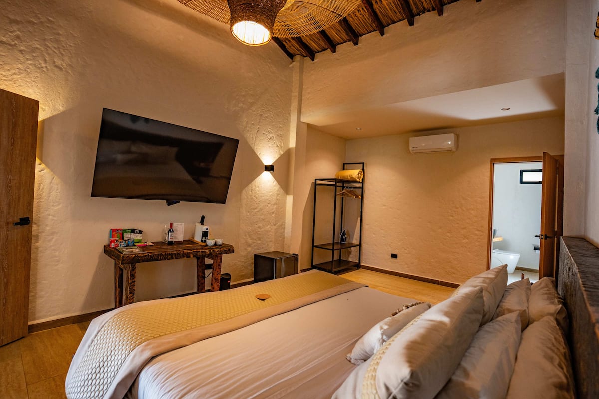 A spacious bedroom with a large bed, a flat-screen TV mounted on the wall, a bedside table with toiletries, and a walk-in closet.