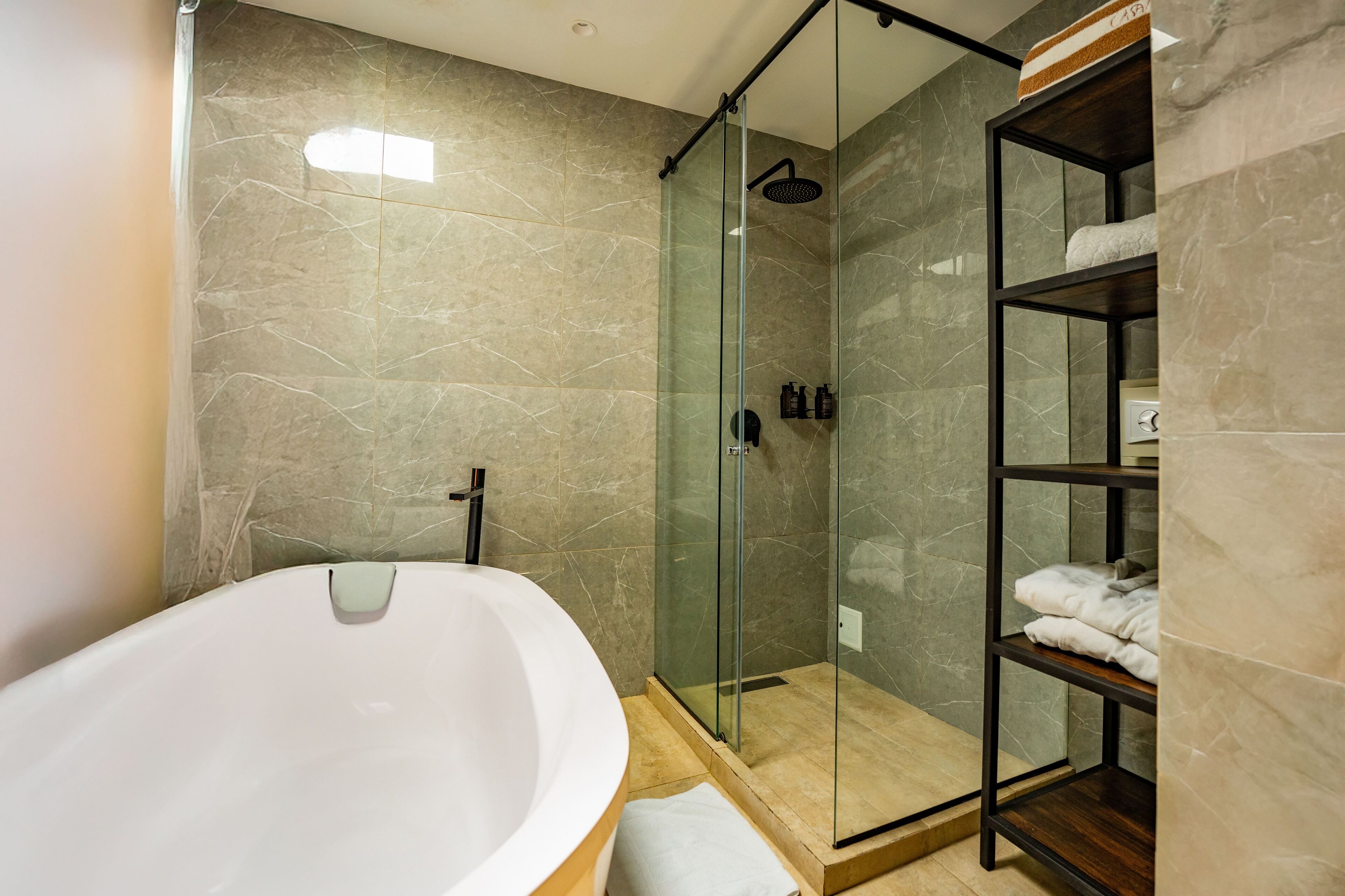 A modern bathroom with a freestanding bathtub, a glass-enclosed shower, and a built-in shelf with towels.