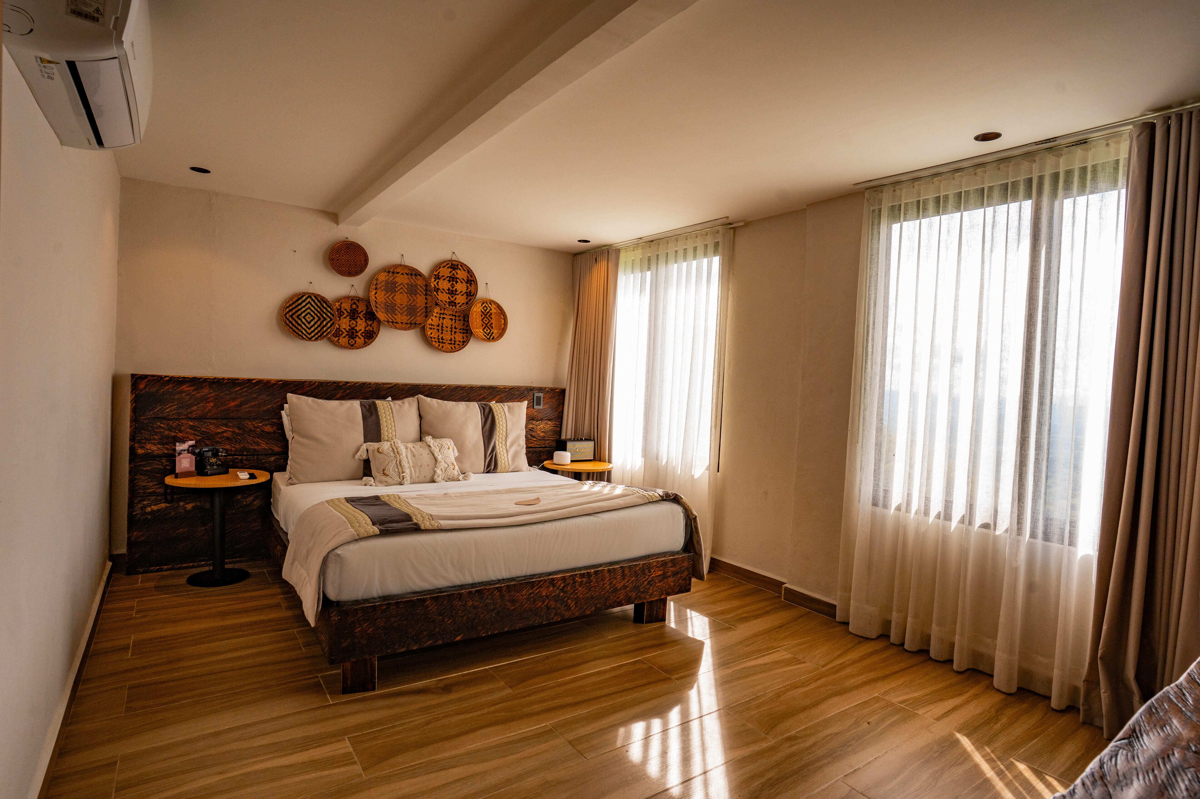 A spacious bedroom with a large bed, wooden headboard, two bedside tables, and a view of the outdoors through sheer curtains.