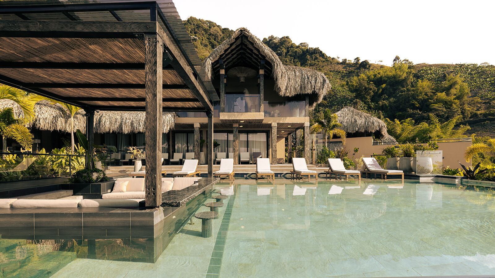 A resort with a swimming pool, lounge chairs, and a thatched-roof building.