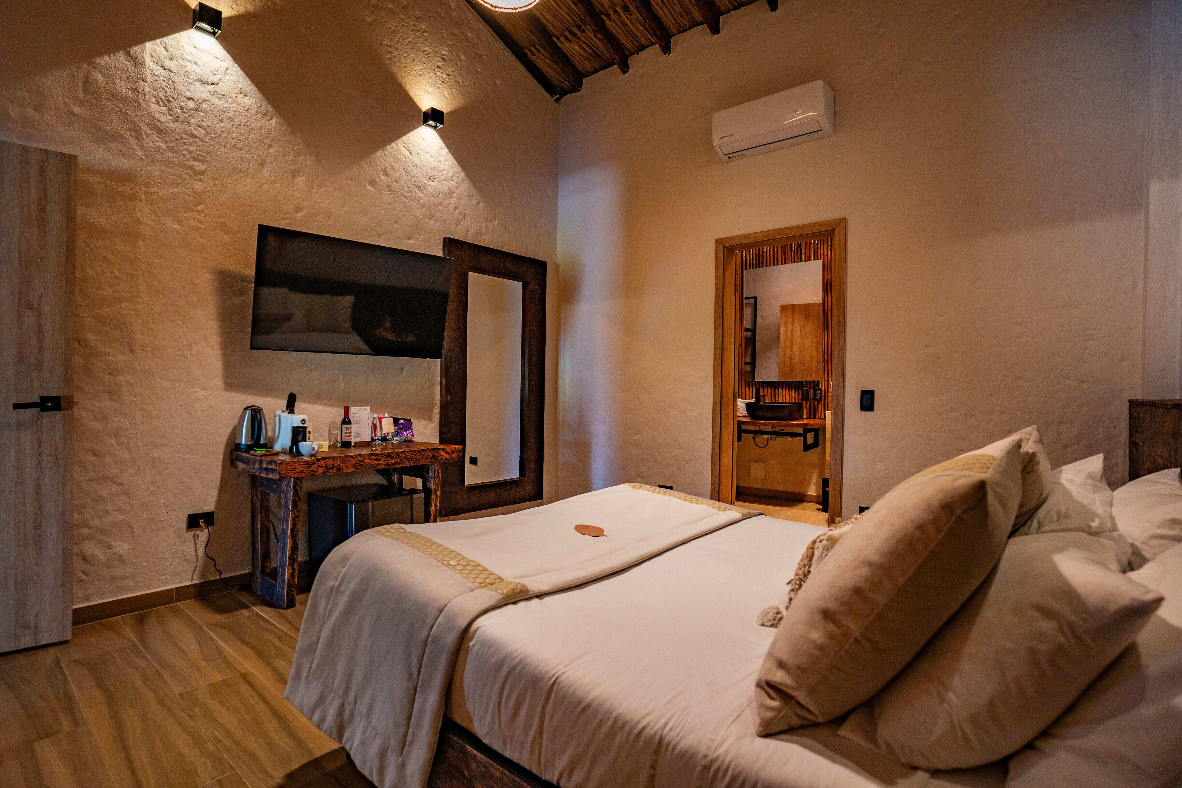 A bedroom with a wooden bed, a bedside table with a lamp, a mirror, and an air conditioning unit on the wall.