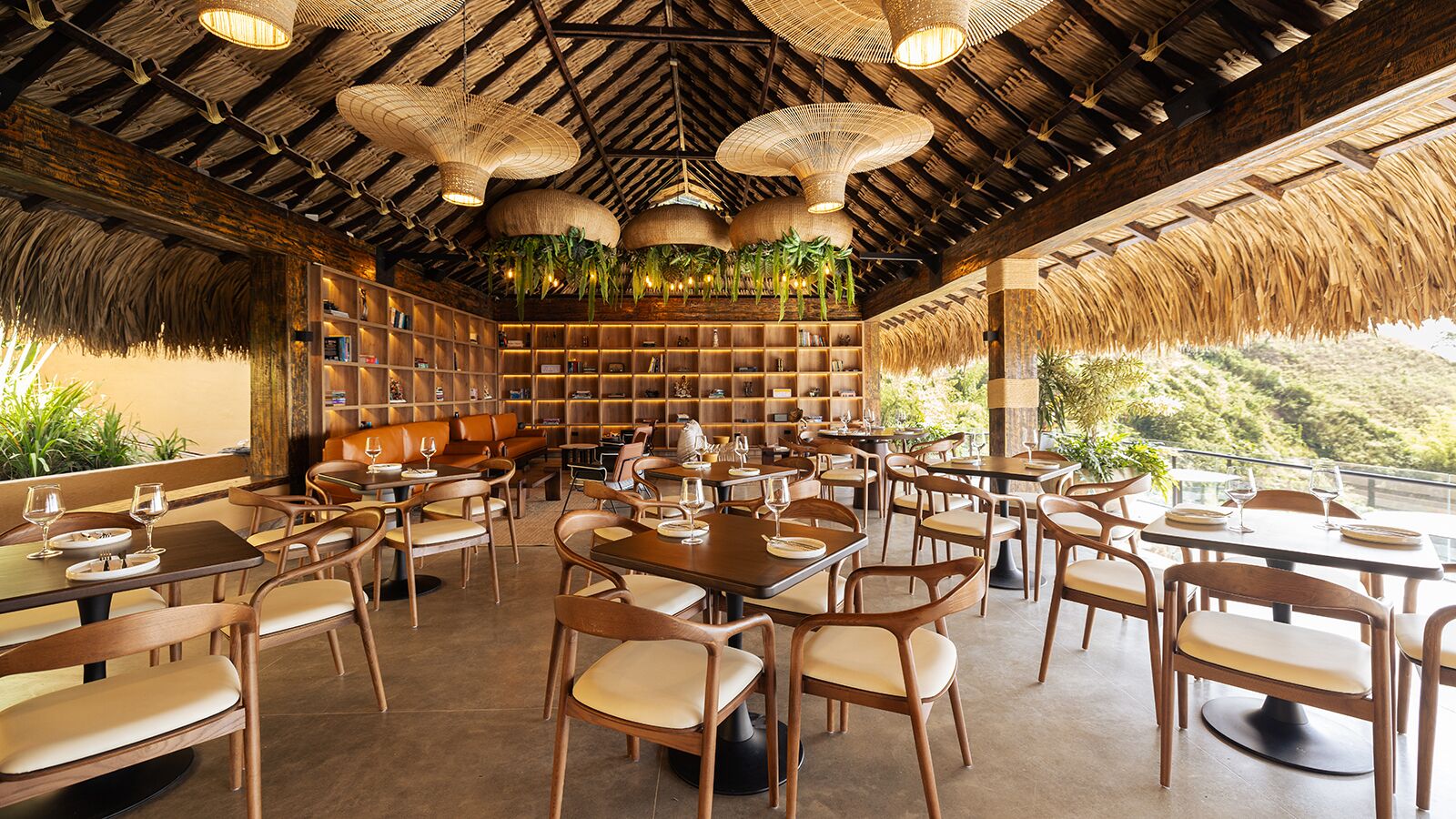 A restaurant with wooden furniture, a thatched roof, and hanging plants.