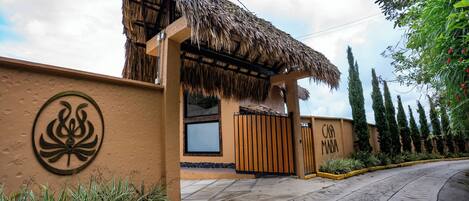 A building with a thatched roof entrance, a wall with a circular emblem, and a gated driveway.