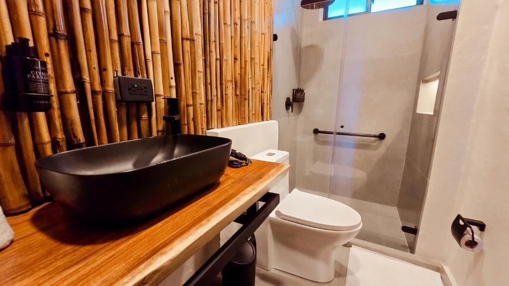 A bathroom with a bamboo wall, a black basin, a white toilet, and a glass shower enclosure.