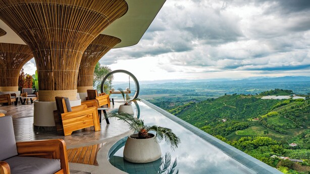 Un área de descanso al aire libre, moderna, con mobiliario de madera, un conjunto de asientos circulares y vistas a un valle exuberante.
