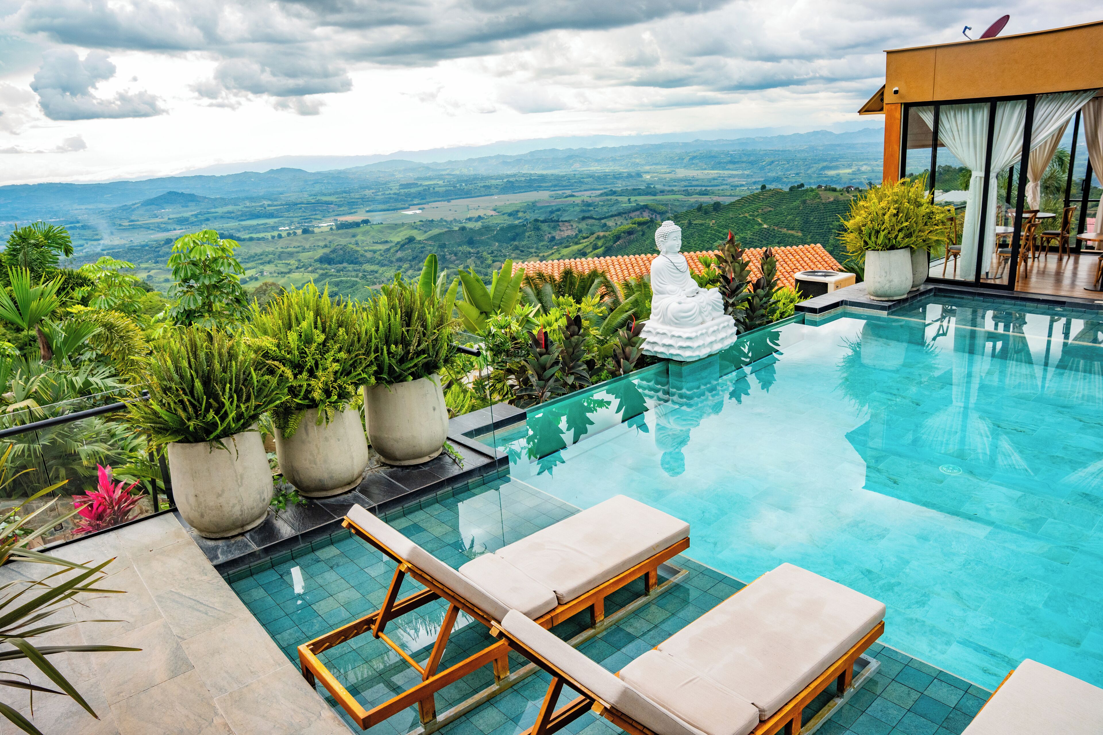 Una piscina con sillones de descanso, plantas en macetas y una estatua de Buda.