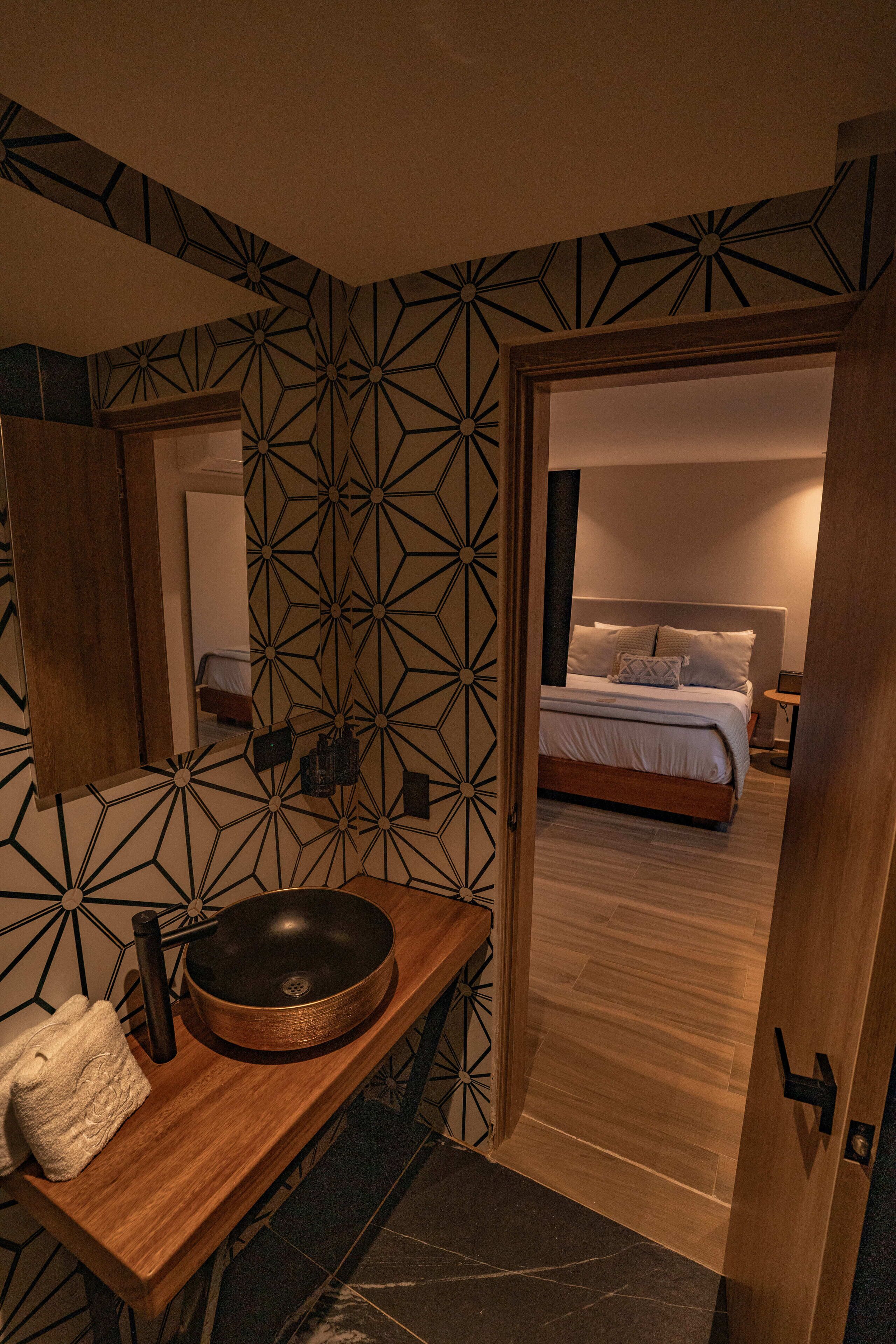 A modern bathroom with a wooden vanity, a large mirror, and a geometric-patterned wall.