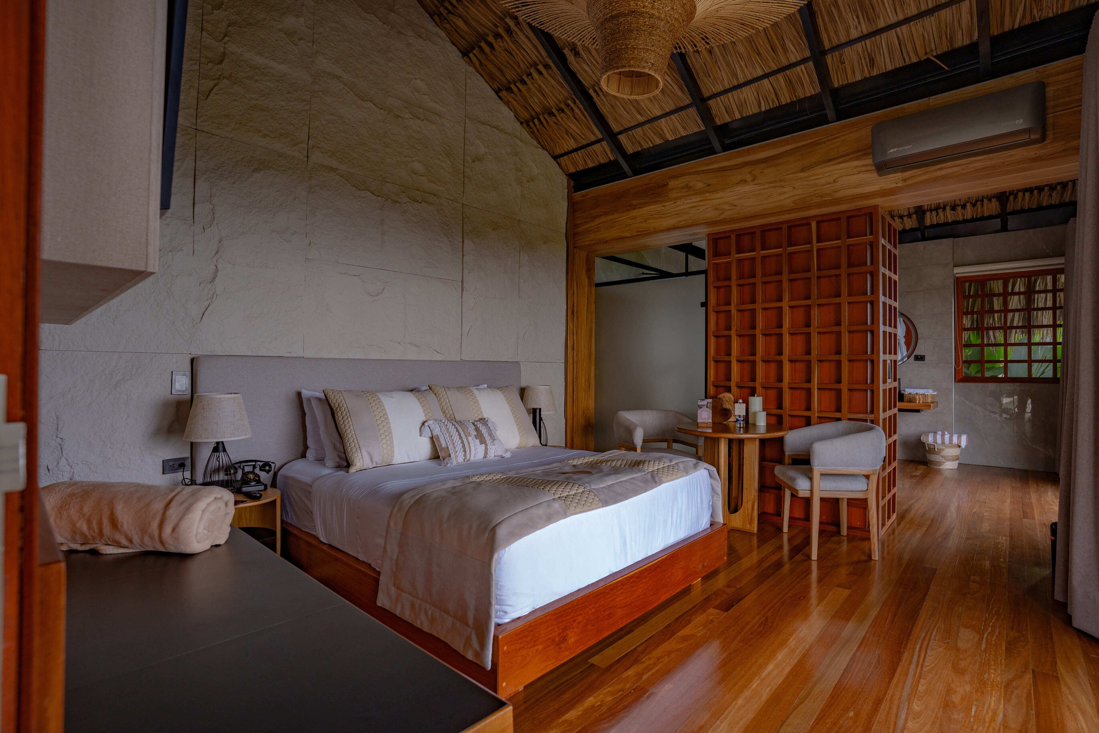A bedroom with a large bed, bedside tables, a chair, a wooden bookshelf, and a ceiling fan.