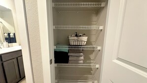 Ein schmaler Flur mit weißen Regalelementen, auf denen gefaltete Handtücher und Pflegeprodukte liegen.