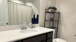 Ein Badezimmer mit einem weißen Waschbecken, dunklen Schränken, einer Toilette, einem Spiegel und einem Ablagefach mit Pflegeprodukten.