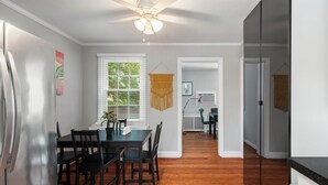 A dining area with a table and chairs, a ceiling fan, and a view into another room.