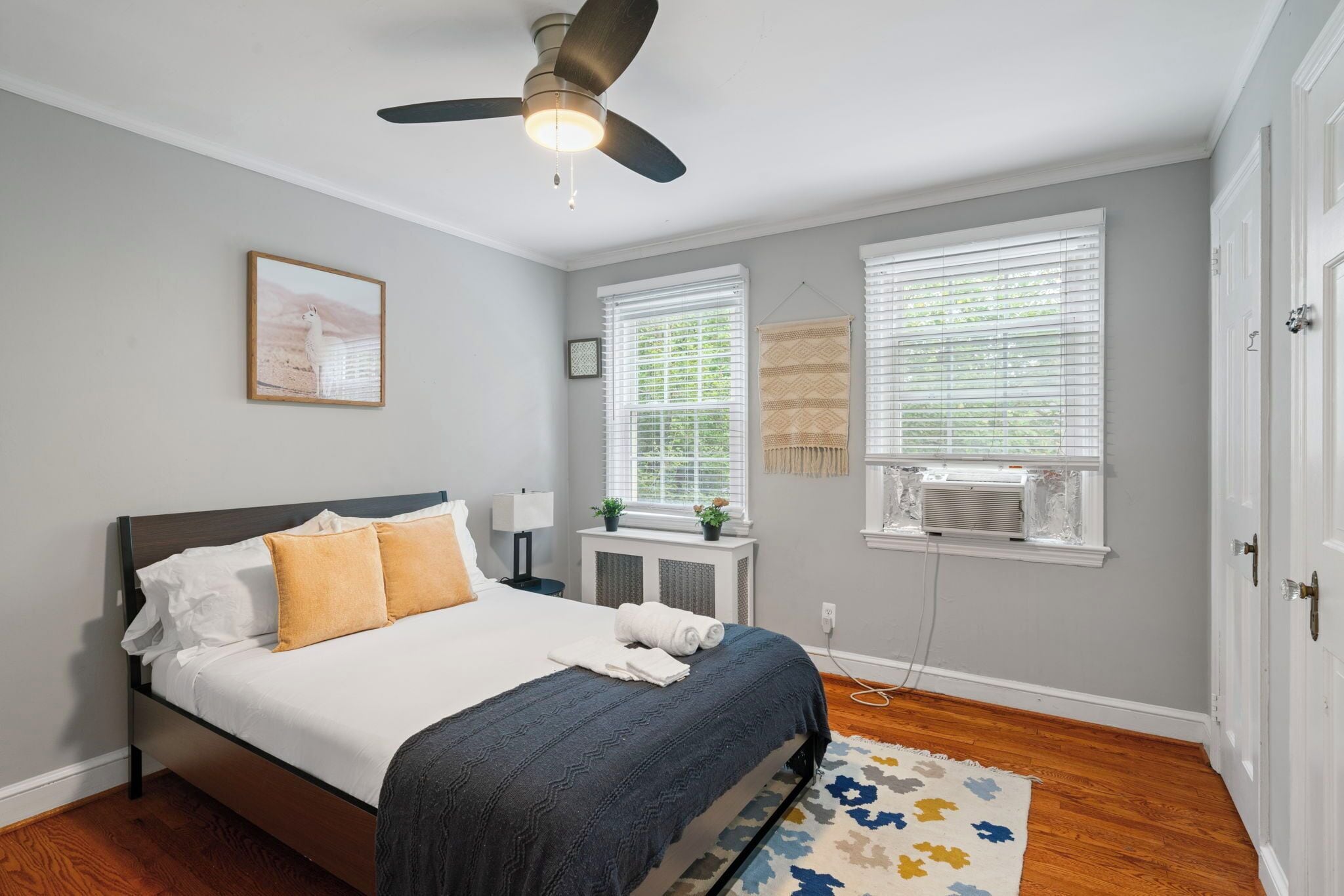 A bedroom with a bed, ceiling fan, windows, and a radiator.
