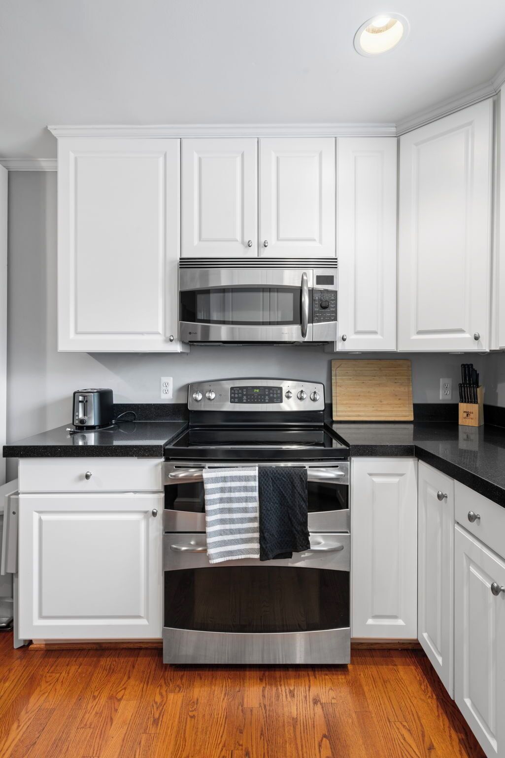 A kitchen with white cabinets, a stainless steel microwave, an oven, and a toaster.