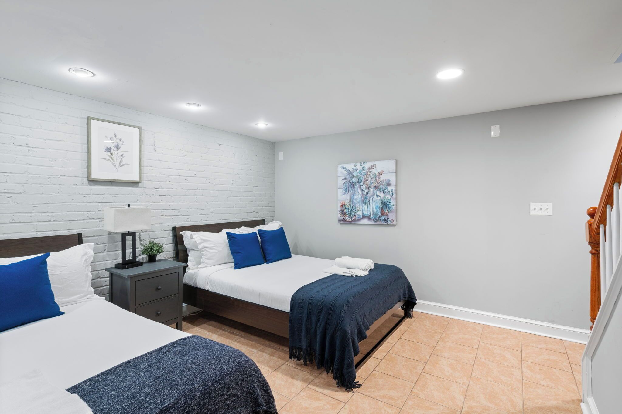 A bedroom with two beds, a nightstand, a lamp, and artwork on the walls.