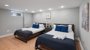 A bedroom with two beds, a window, and a brick wall.