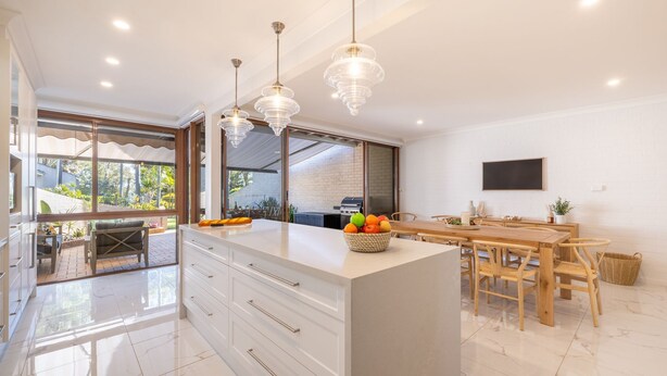 A modern kitchen with a large island, white cabinetry, and a dining area with wooden furniture. - The Moorings 22, 4 Cromarty Rd - stunning townhouse with water views (Soldiers Point)
