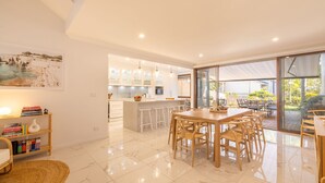 A modern kitchen with white cabinets and a central island, a dining area with wooden chairs, and a view of a patio with outdoor furniture. - The Moorings 22, 4 Cromarty Rd - stunning townhouse with water views (Soldiers Point)