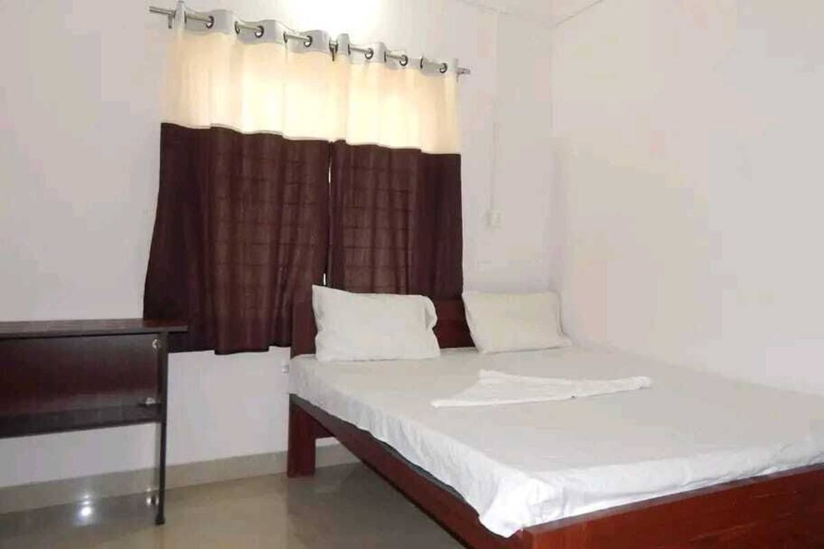 A bedroom with a single bed, a wooden headboard, a nightstand, and a window with curtains.