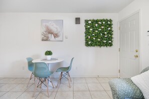 Un coin repas avec une table ronde, deux chaises de couleur turquoise, une petite plante en pot et une œuvre d’art florale encadrée accrochée au mur.