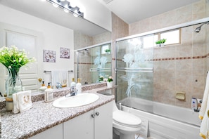 Une salle de bain moderne avec un comptoir en granit, un lavabo blanc, une cabine de douche en verre et des toilettes.