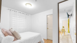 Une chambre à coucher comprenant un lit, une table de chevet, une fenêtre avec des stores et une porte donnant sur une autre pièce.