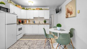 Une cuisine compacte avec des meubles blancs, un four à micro-ondes et un évier. On y trouve également un coin repas avec une table ronde et des chaises vertes.