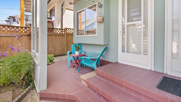 Une terrasse couverte avec une petite table et des chaises, une clôture en bois et une porte dotée de panneaux en verre dépoli.