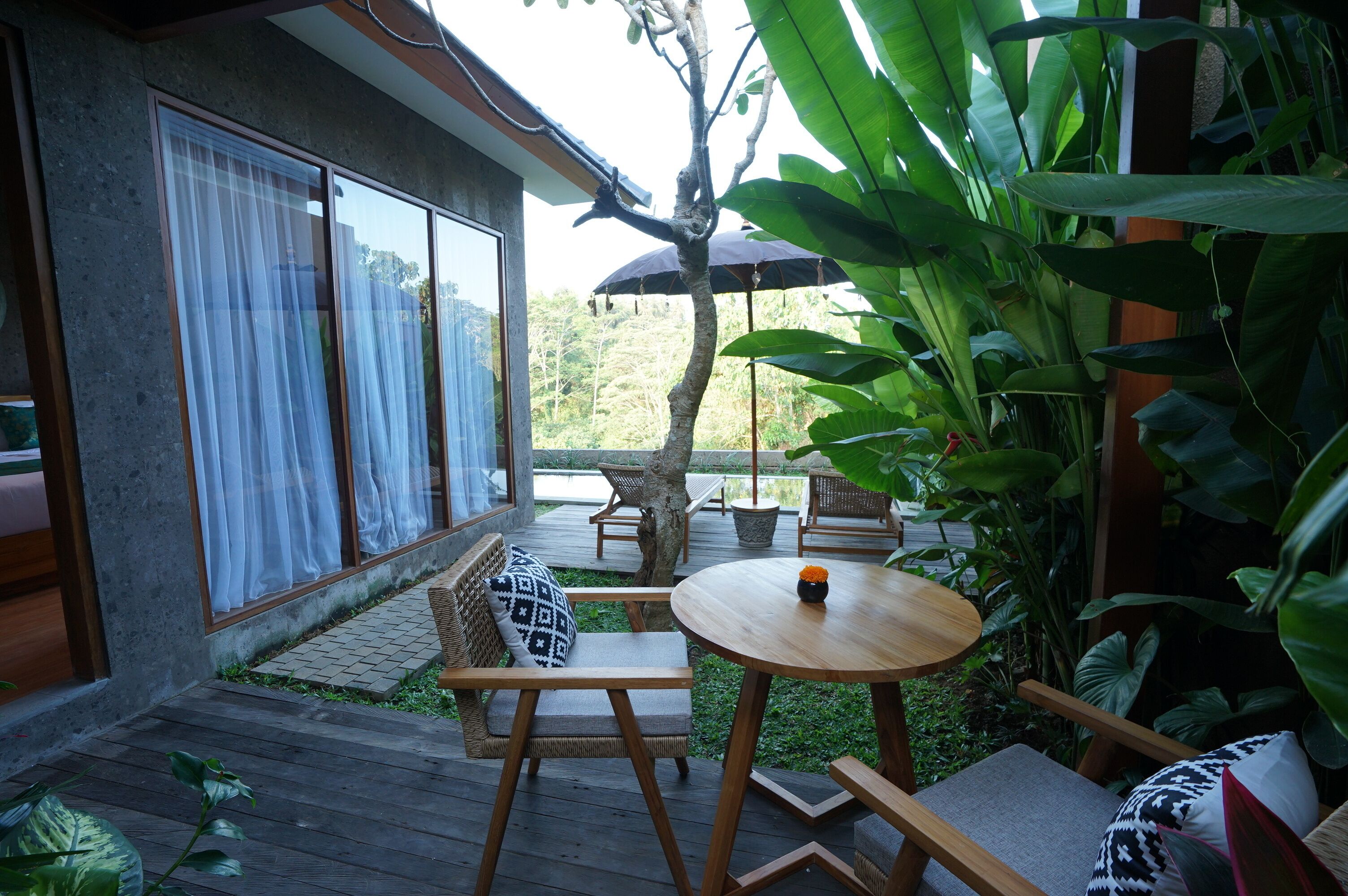 Um deck de madeira com móveis de exterior, uma mesa redonda e um grande guarda-sol.