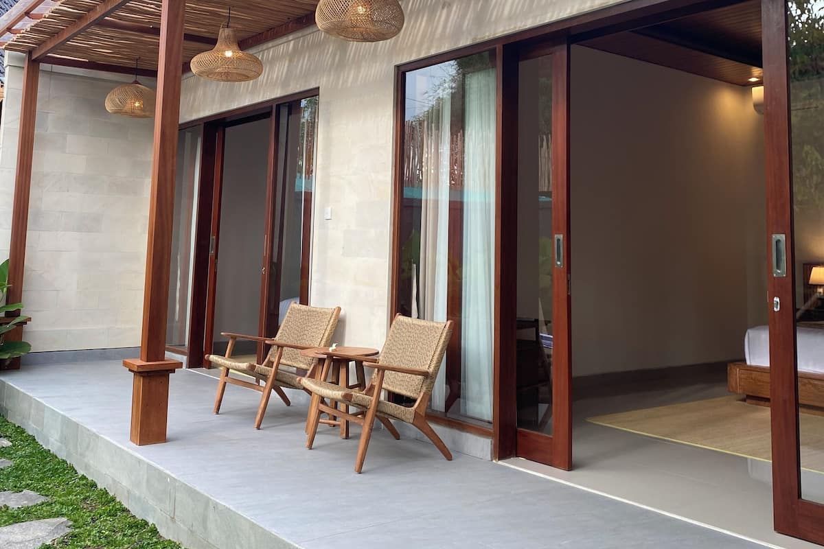 A modern outdoor seating area with wicker chairs and a table, a wooden pergola, and a glass door leading to a room.