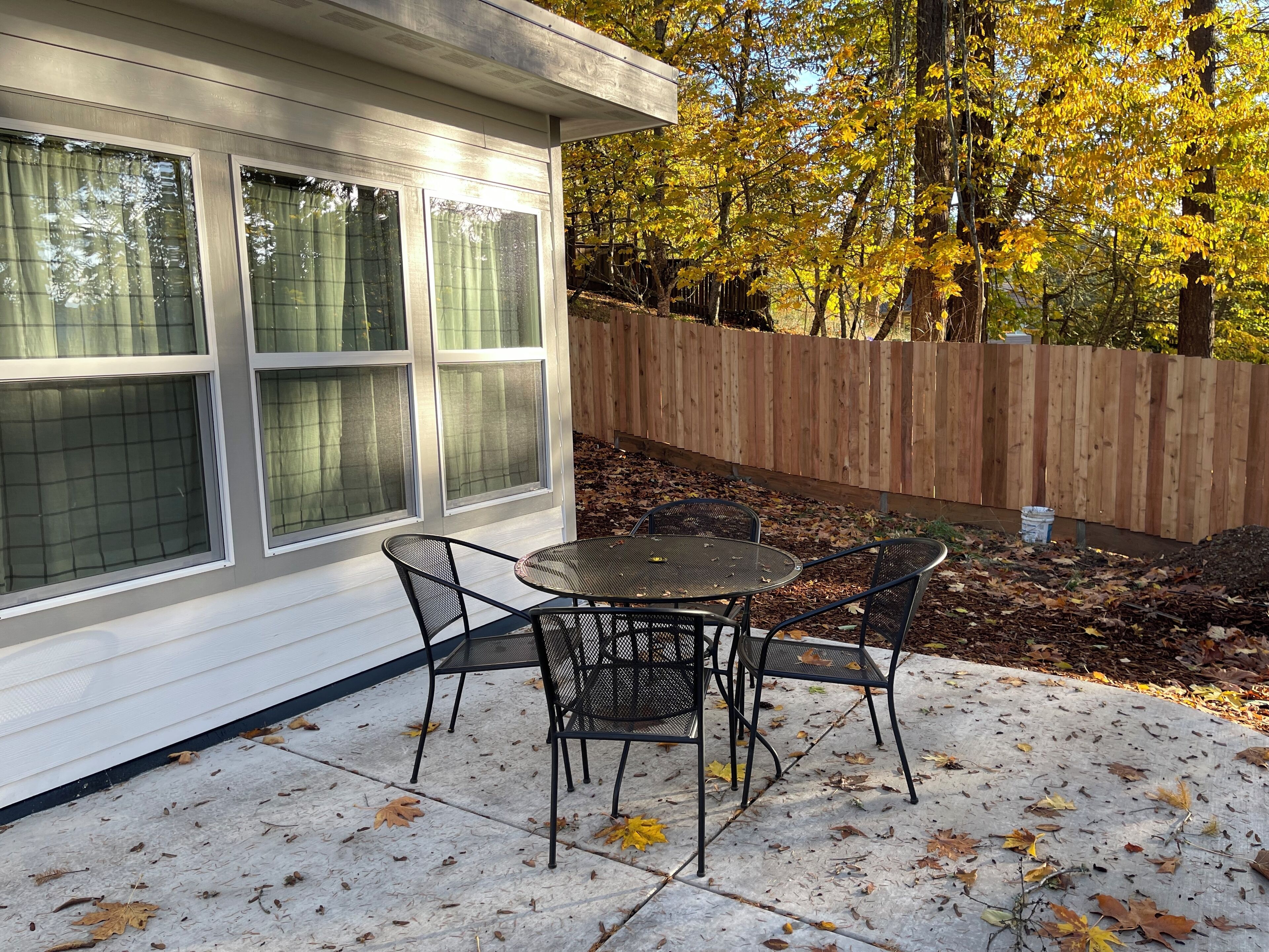 Une terrasse avec une table et des chaises, une clôture en bois et des arbres aux feuilles jaunes.