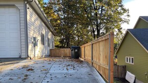 A residential driveway with a concrete path, wooden fence, and a garage. - Kamal's Comfy Relaxation Zone (Eugene)