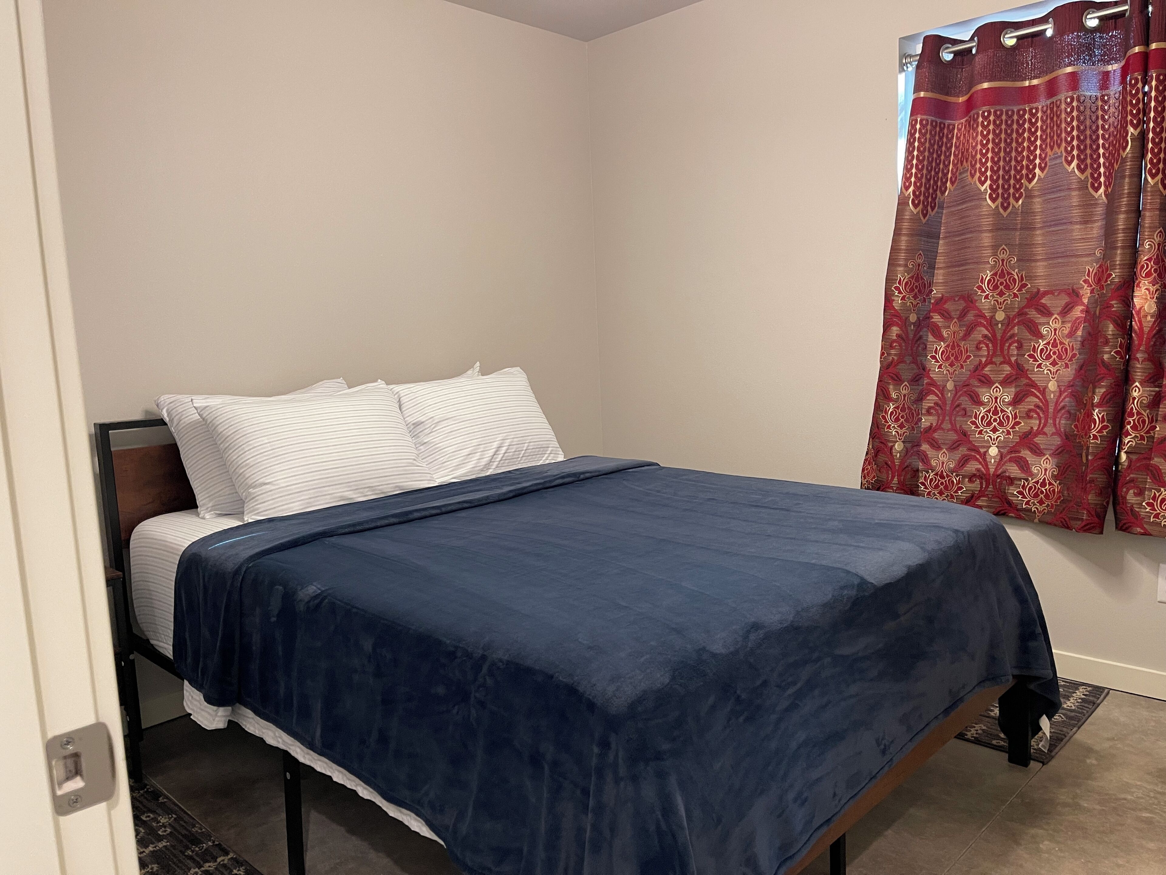 Una cama individual con colcha azul oscuro, almohadas a rayas blancas y cabecero de madera.