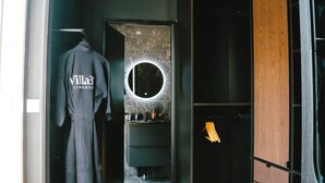 A hallway with a wooden floor, a robe hanging on a rack, a mirror with a circular frame, and a wardrobe. - Villa37 (Limoges)