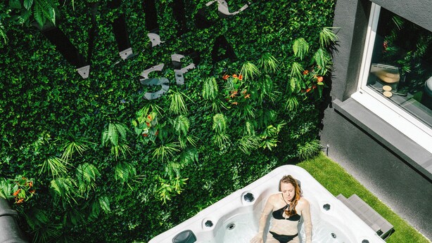 A person in a hot tub with a lush green hedge in the background. - Villa37 (Limoges)