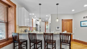 Une cuisine avec des chaises en bois, des armoires blanches et des luminaires suspendus.