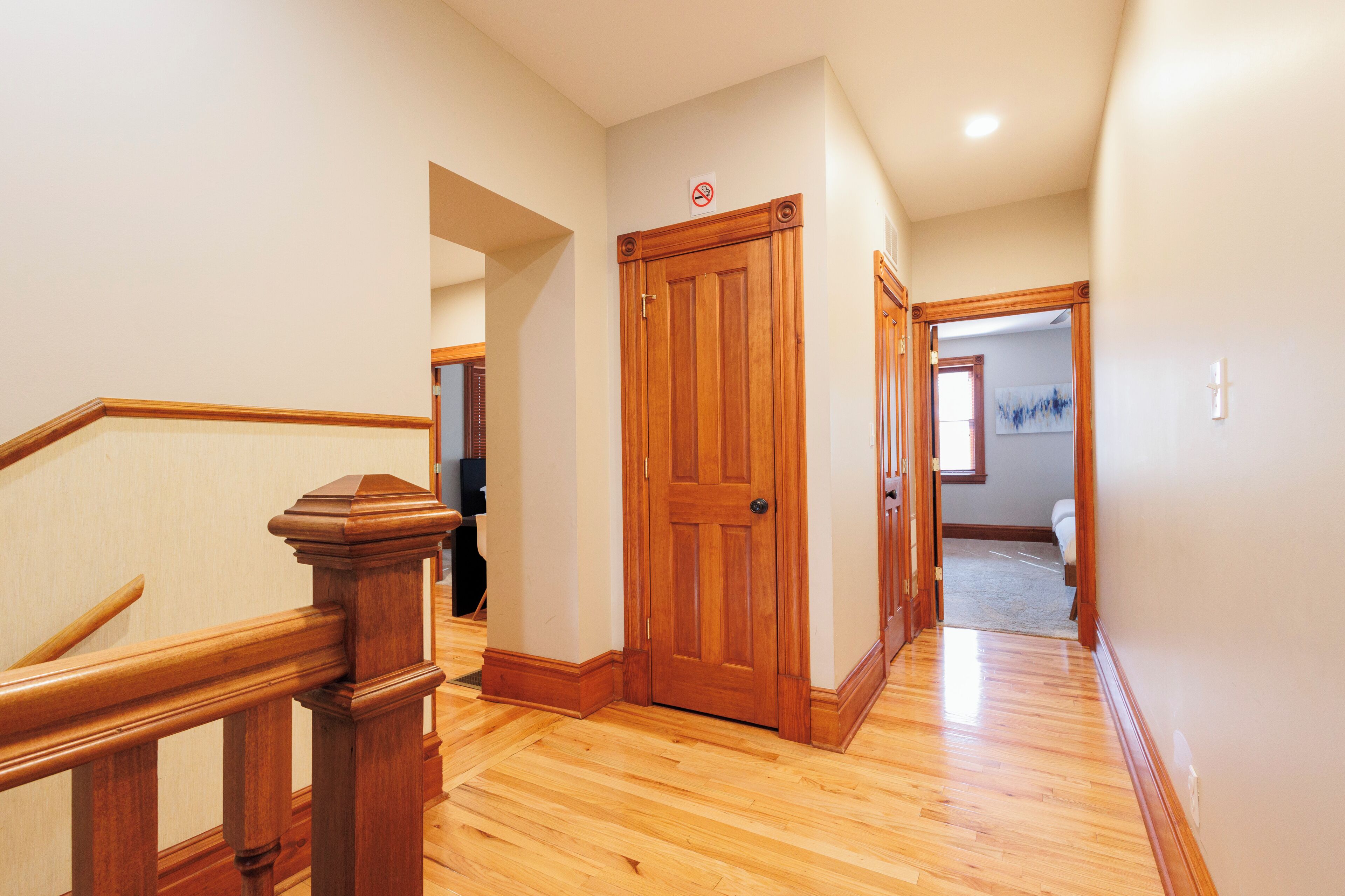 A hallway with wooden flooring, a wooden door, and a staircase with a wooden handrail.