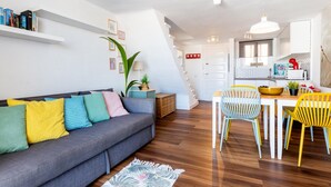 A modern living room with a grey sofa, colorful cushions, a wooden dining table with yellow chairs, and a staircase leading to the kitchen. - 327 Parque Santiago II, sea view, 2 bedroom, 2 bathroom, wifi (Playa de las Américas)