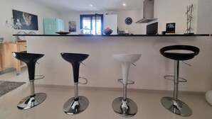 A modern kitchen with four bar stools, a refrigerator, a clock, and a window with curtains. - Superb villa with a private pool (Saint-Nazaire-d'Aude)