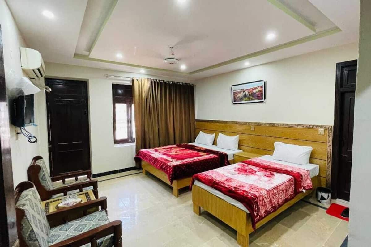 A hotel room with two beds, a wooden headboard, a small table with a chair, and a window with curtains.