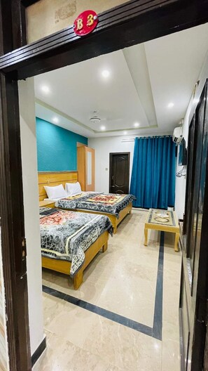 A hotel room with two beds, a small table, a TV, and a bathroom door. - Hotel The Queen (Rawalpindi)