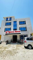 Ein Hotel namens "Queen Hotel" mit einer modernen Ziegel-Fassade, zahlreichen Fenstern und einem gepflasterten Eingangsbereich mit parkenden Fahrzeugen.