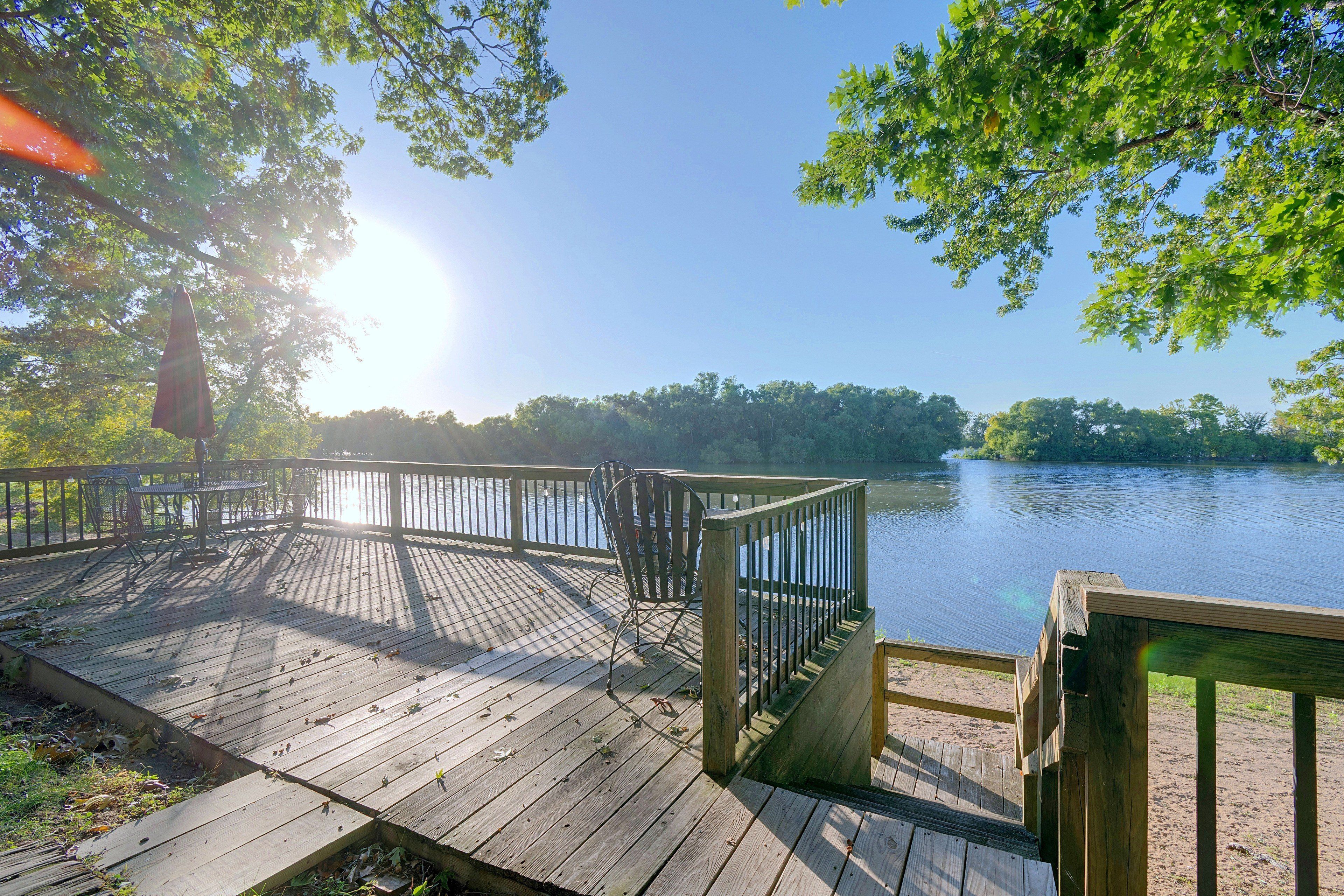 A wooden deck with metal railings overlooking a calm lake, surrounded by trees.