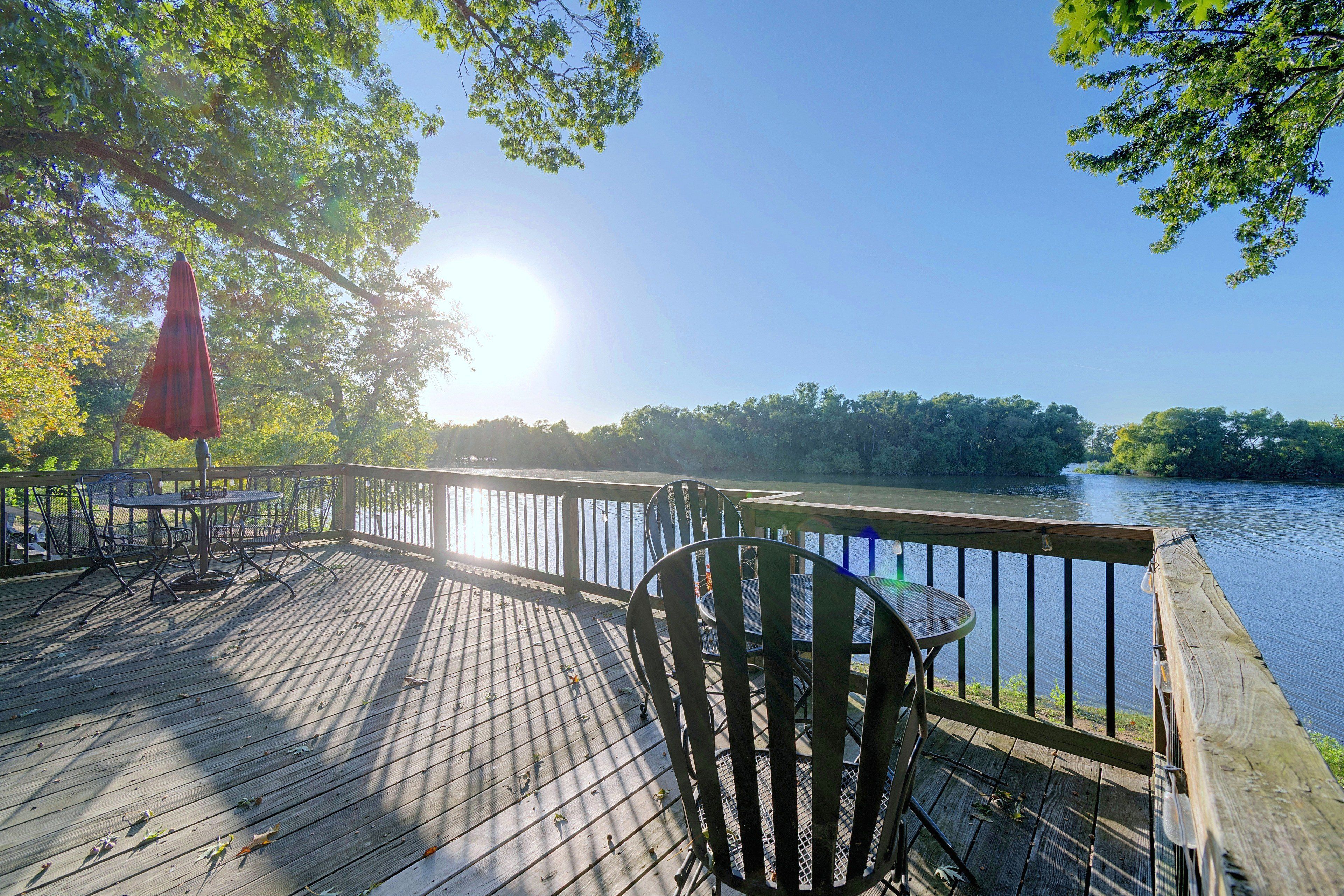 A wooden deck with metal chairs and tables, overlooking a calm body of water.
