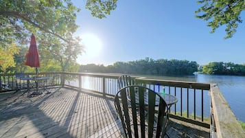 A wooden deck with metal chairs and tables, overlooking a calm body of water.