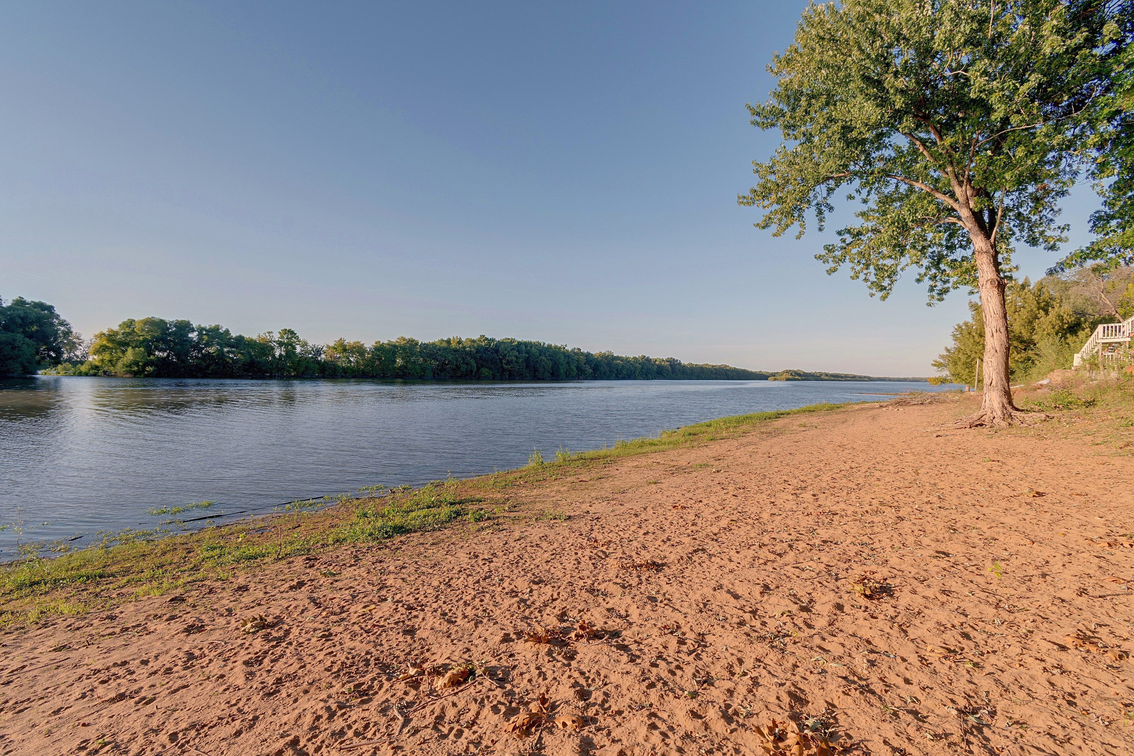 A riverbank with a sandy shore and a tree on the right.