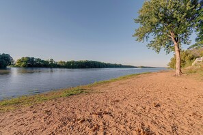 Une rive avec un rivage sablonneux et un arbre sur la droite.