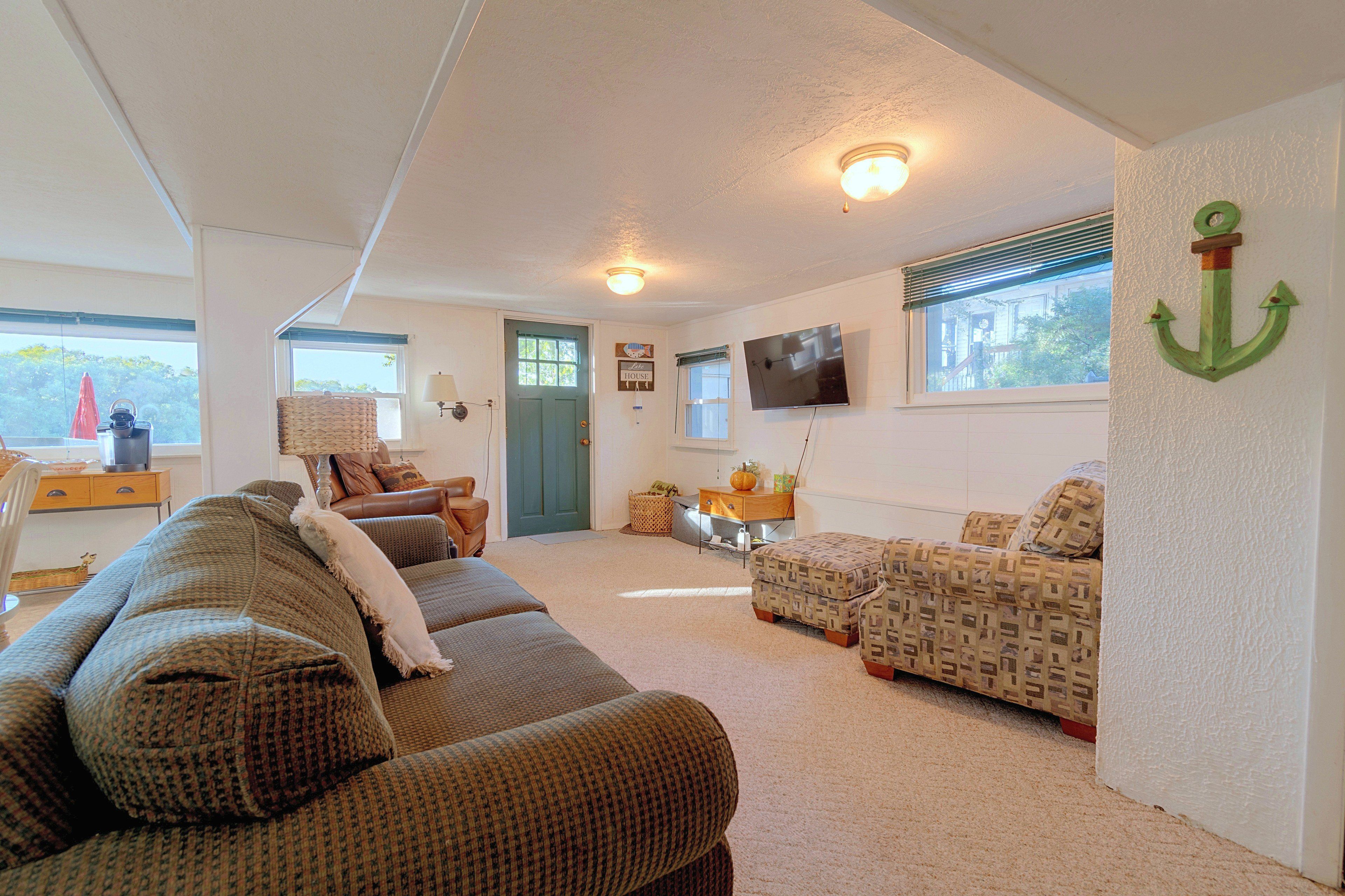 A cozy living room with a sofa, a patterned ottoman, a television, and a decorative anchor on the wall.