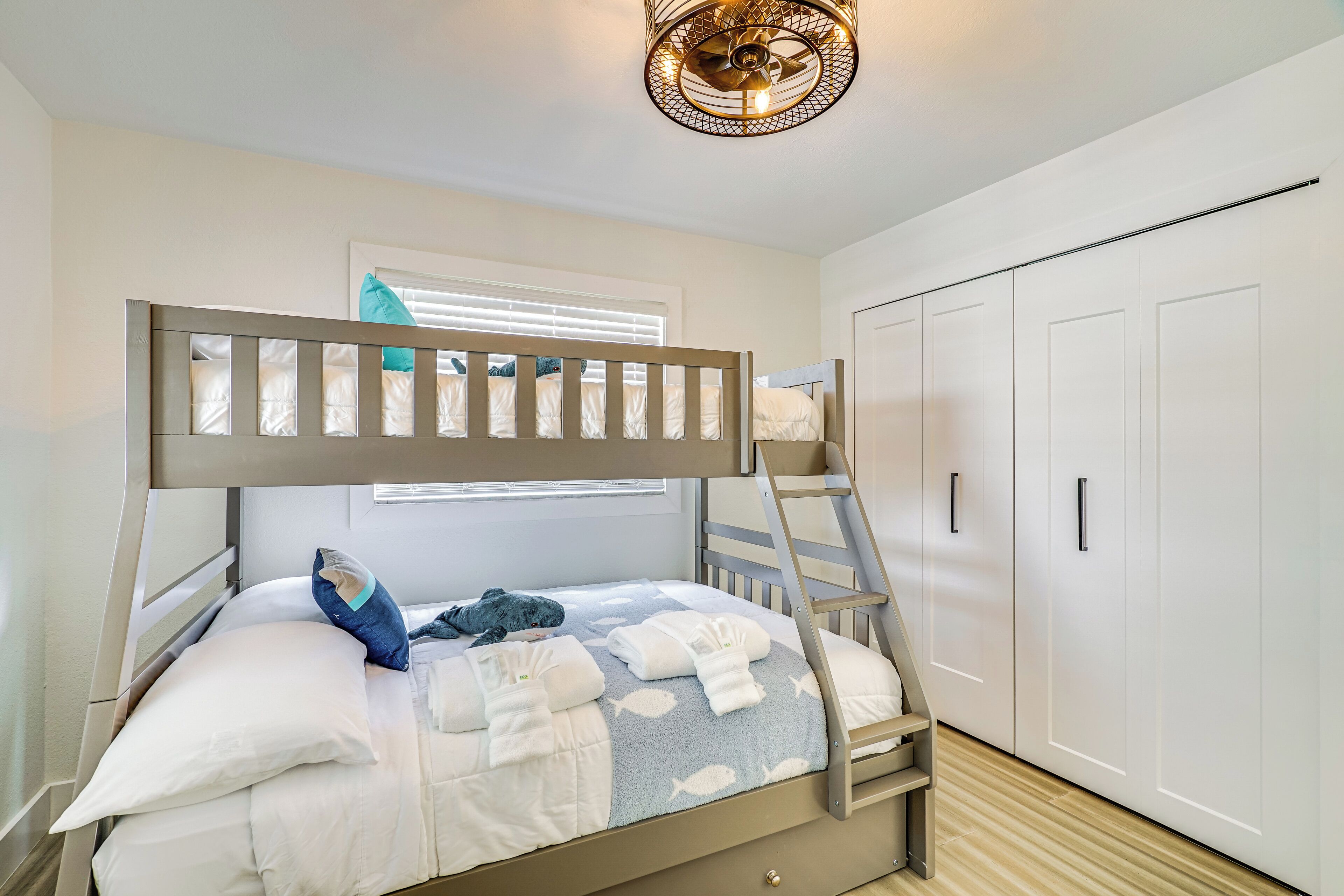 A bunk bed with a ladder, a window with blinds, and a wardrobe with handles.