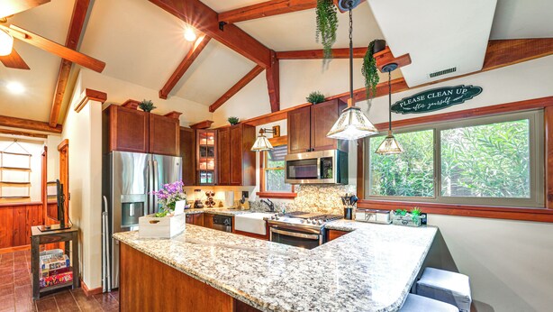 Una cocina con armarios de madera, encimeras de granito, electrodomésticos de acero inoxidable y plantas colgantes.